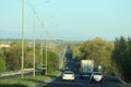 A long four-lane highway with busy traffic with a row of street lights among the trees in the early spring morning Royalty Free Stock Photo