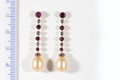 Long gold earrings with diamonds, rubies and pearls, on a white background next to the ruler Royalty Free Stock Photo