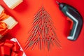 Long golden self-tapping screws, laid out in shape of Christmas tree, screwdriver, and gift boxes on red background Royalty Free Stock Photo