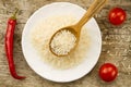 Long grain rice in a wooden spoon on a background plates, chili pepper, cherry tomato. Healthy eating, diet