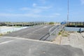 Long gray wooden ramp leading from an asphalt road to the boardwalk and beach