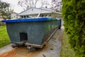 A long green empty dumpster full of debris is seen in the driveway in front of a home being renovated