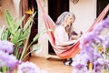 Long grey and white hair adult woman alternative look have relax at home in the garden sitting on a coloured hammock alone