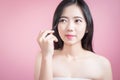 Long hair asian young beautiful woman applying cosmetic powder brush on smooth face isolated over pink background. natural makeup. Royalty Free Stock Photo