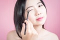 Long hair asian young beautiful woman applying cosmetic powder brush on smooth face isolated over pink background. natural makeup. Royalty Free Stock Photo