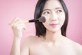 Long hair asian young beautiful woman applying cosmetic powder brush on smooth face isolated over pink background. natural makeup. Royalty Free Stock Photo