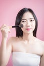 Long hair asian young beautiful woman applying cosmetic powder brush on smooth face isolated over pink background. natural makeup.