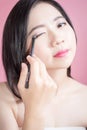 Long hair asian young beautiful woman applying cosmetic powder brush on smooth face isolated over pink background. natural. Royalty Free Stock Photo