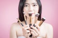 Long hair asian young beautiful woman smile and fun, touch her face and hold cosmetic powder brush set, isolated over pink. Royalty Free Stock Photo