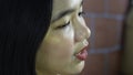 Long-haired beautiful Asian girl standing near the brick wall reciting homework narration lesson assignment.