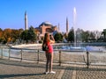 Long-haired blonde take photographs of fountain near the Church of the Holy Wisdom by phone on Sultanahmet Square in Istanbul.