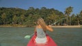 Long haired blonde woman with sunglasses rows bright pink canoe along sea bay water to beach with growing palms. Royalty Free Stock Photo