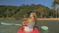 Long haired blonde woman with sunglasses rows bright pink canoe along sea bay water to beach with growing palms. Royalty Free Stock Photo