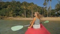 Long haired blonde woman with sunglasses rows bright pink canoe along sea bay water to beach with growing palms. Royalty Free Stock Photo