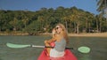 Long haired blonde woman with sunglasses rows bright pink canoe along sea bay water to beach with growing palms. Royalty Free Stock Photo