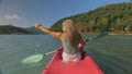 Long haired blonde woman with sunglasses rows bright pink canoe along sea bay water to beach with growing palms. Royalty Free Stock Photo