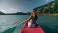 Long haired blonde woman with sunglasses rows bright pink canoe along sea bay water to beach with growing palms. Royalty Free Stock Photo