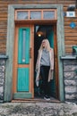 Long haired blonde woman wearing a sand coat with wool sweater, and black jeans, standing on a stairway behind old fashioned house Royalty Free Stock Photo