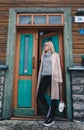 Long haired blonde woman wearing a sand coat with wool sweater, and black jeans, standing on a stairway behind old fashioned house Royalty Free Stock Photo