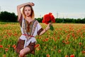 Long-haired blonde young woman in a white short dress on a field of green wheat and wild poppies Royalty Free Stock Photo