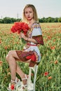 Long-haired blonde young woman in a white short dress on a field of green wheat and wild poppies Royalty Free Stock Photo