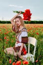 Long-haired blonde young woman in a white short dress on a field of green wheat and wild poppies Royalty Free Stock Photo