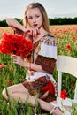 Long-haired blonde young woman in a white short dress on a field of green wheat and wild poppies Royalty Free Stock Photo