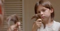 A long-haired boy holds a bunch of hair in his hands and throws it down.