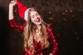 Long-haired brunette woman taking off santa claus hat after photoshoot. Indoor portrait of graceful curly female model