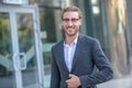 Long-haired businessman in eyeglasses standing outside business center, unbottoning his jacker Royalty Free Stock Photo