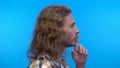 Profile portrait.long-haired curly man on an isolated blue background. Man tells a secret and shows a shhh gesture