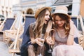 Long-haired excited girl telling her friend last gossips during rest outside. Outdoor portrait of adorable stylish