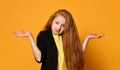 Ginger teenage girl in black jacket and yellow t-shirt. Acting like she does not know, posing on orange background. Close up