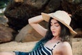 Long haired girl In a hipster hat and striped swimsuit relax on tropical beach, background of stones. Royalty Free Stock Photo