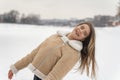 Long-haired girl in trendy beige sheepskin coat have fun in snowy clearing. Woman rejoices in frosty winter day