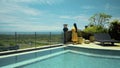 Long-haired girl walking in the backyard with a green garden, pool with blue clean water and blue sky in a beautiful long yellow Royalty Free Stock Photo