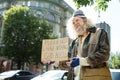 Long-haired homeless man standing near traffic asking for help
