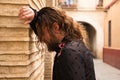 long-haired man dancing flamenco with black shirt and red roses rests his head on the wall of a narrow street typical of seville.