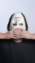 A long-haired man holds a white mask upside down near his face. The concept of hiding a person, peeping, mental problems, a split