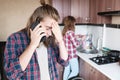 A long-haired man is upset talking on the phone or calling a food and drug delivery service home standing in the kitchen Royalty Free Stock Photo