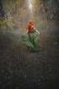 A long-haired red-haired elf girl runs away into the distance through the misty autumn forest. A fairy woman with long Royalty Free Stock Photo