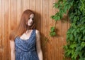 Long haired redhead women leaning against plank background with green leaves of ivy or grape over Royalty Free Stock Photo