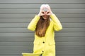 Long-haired stylish girl in a yellow coat and hat looks through binoculars Royalty Free Stock Photo