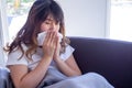 Long haired woman sitting on the sofa is suffering from flu, cough and sneezing. Sitting in a blanket because of high fever and Royalty Free Stock Photo