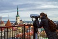 Long-haired woman tourist with a backpack looking through binoculars historical sights of Tallinn city. Royalty Free Stock Photo