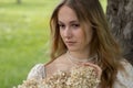 Long-haired young blonde girl with flowers in her hands against the background of a summer green field Royalty Free Stock Photo