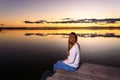 Long-haired young woman relaxing admiring the golden sunset on a beautiful pier by a natural lake Royalty Free Stock Photo