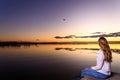 Long-haired young woman relaxing admiring the golden sunset on a beautiful pier by a natural lake Royalty Free Stock Photo