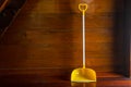 Long handle plastic yellow dustpan leaning against wooden wall