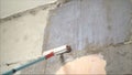 Long handle roller brush applying white primer paint on concrete wall with glass blocks in part of door frame, building and home